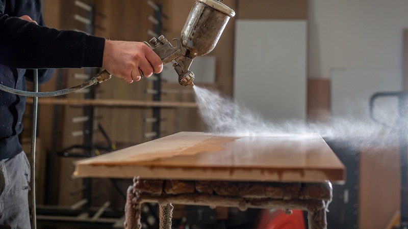 A man applying a layer of varnish to a garden table.